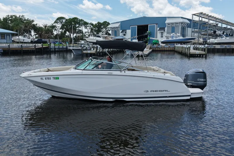 Slide: The Image of 2019 Regal 23 OBX boat on calm water near marina, featuring Yamaha outboard motor. - 6