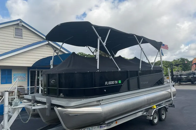 Slide: The Image of 2023 Crest Classic DLX 220 SLC pontoon boat on trailer, parked near a building. - 9