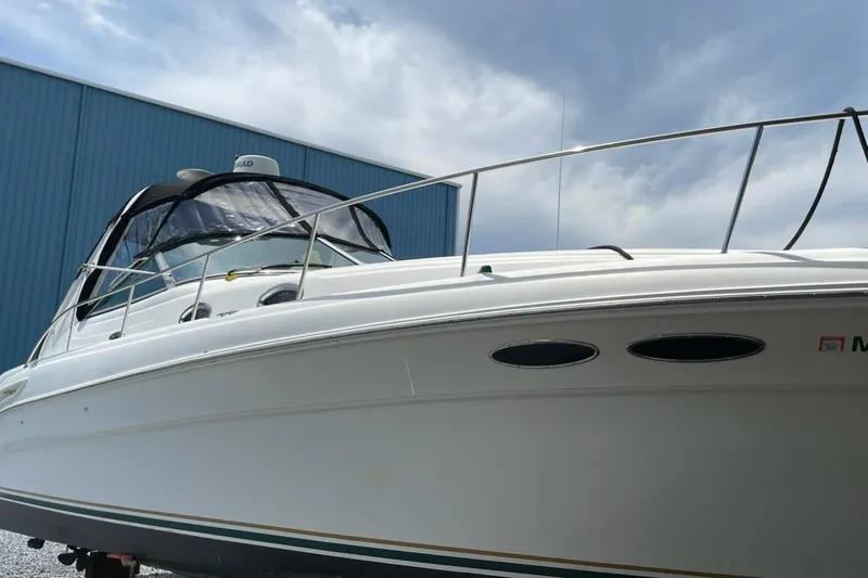 Slide: The Image of 2000 Sea Ray 290 Sundancer boat docked near a blue building under cloudy sky. - 1