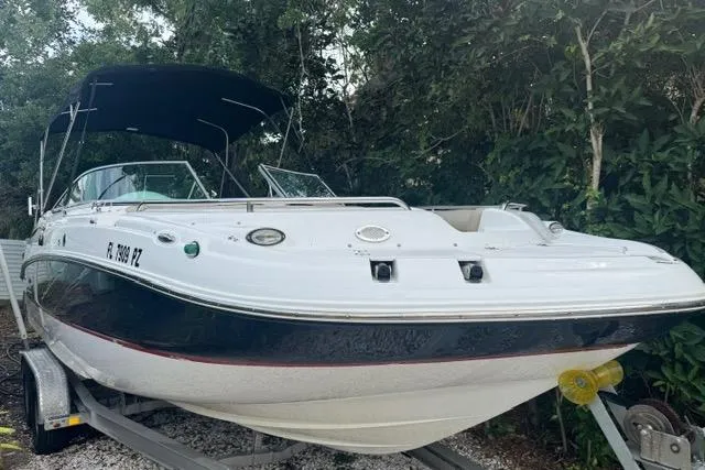 The Image of 2015 Hurricane SunDeck 2400 OB boat on trailer, parked near lush greenery. - 0