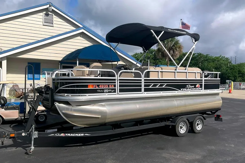 The Image of 2021 Sun Tracker Fishin' Barge 20 DLX on trailer in front of building. - 0