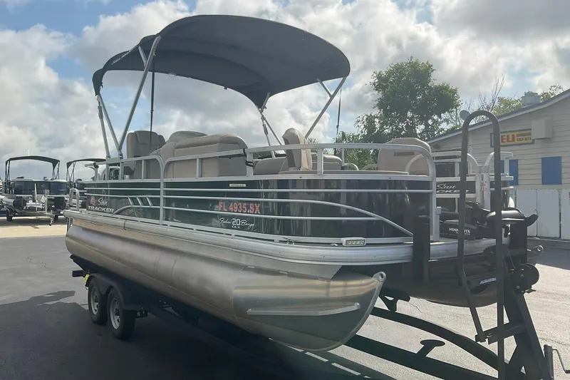 Slide: The Image of 2021 Sun Tracker Fishin' Barge 20 DLX pontoon boat on trailer, parked outdoors. - 2