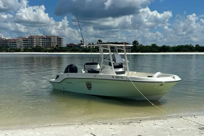The Image of 2023 Bayliner Trophy T22CC boat anchored on a sandy shore under a partly cloudy sky. - 0