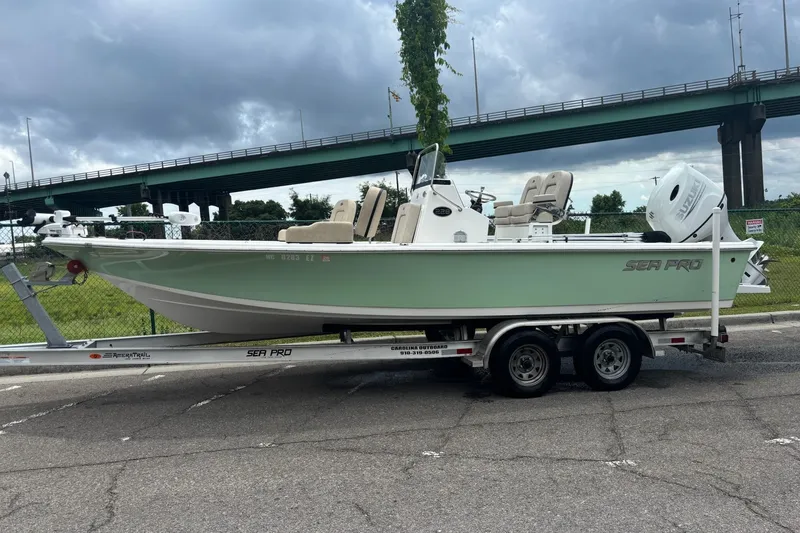 The Image of 2023 Sea Pro 228 Bay boat on trailer, parked near a bridge under cloudy skies. - 1