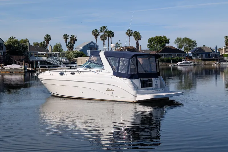 Slide: The Image of 2003 Rinker Fiesta Vee 342 boat on calm water, surrounded by waterfront homes and palm trees. - 1