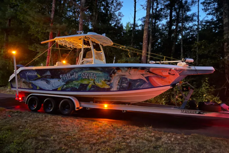 Slide: The Image of 2005 Angler 2700CC boat with vibrant fish mural on trailer at dusk. - 5