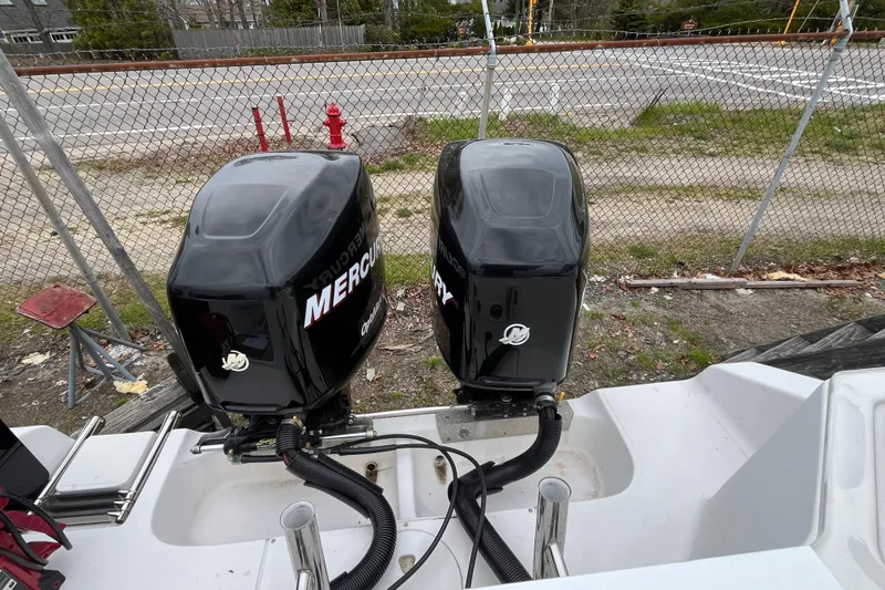 Slide: The Image of Twin Mercury outboard engines on a 2005 Angler 2700CC boat, parked near a chain-link fence. - 7