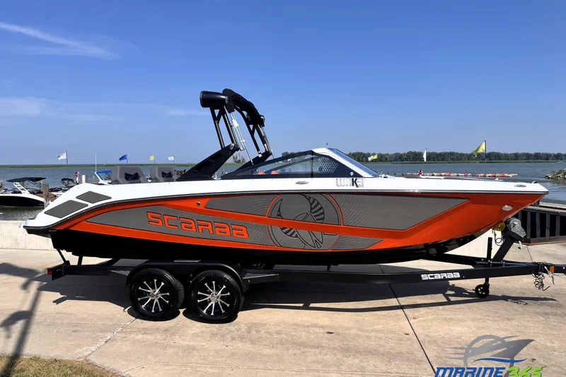 The Image of 2026 Scarab 235 LX Wake boat on trailer by the waterfront, vibrant orange and gray design. - 0