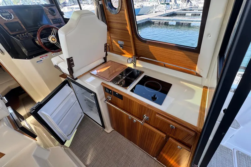 Slide: The Image of 2026 Ranger Tugs R-25 interior with kitchenette, featuring stove, sink, and open fridge. - 18