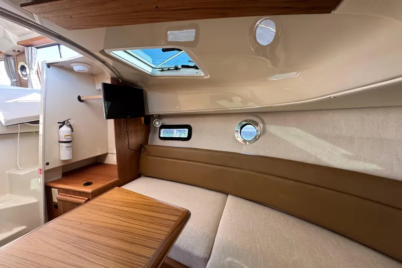 Slide: The Image of 2026 Ranger Tugs R-25 interior cabin with seating, table, and porthole window. - 24