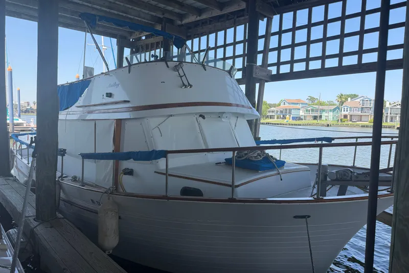 The Image of 1978 Albin 36 Trawler docked in a covered marina, with waterfront homes in the background. - 1