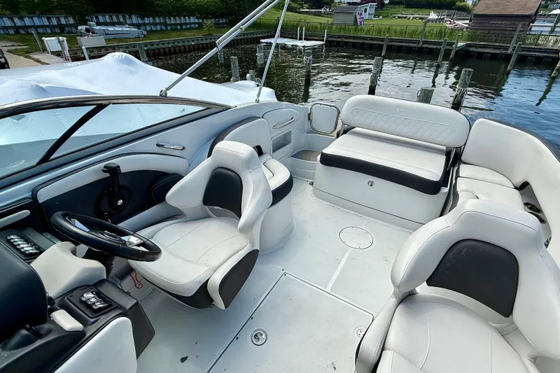 Slide: The Image of 2020 Crownline Eclipse E235 boat interior with white seating and steering wheel, docked by the water. - 14