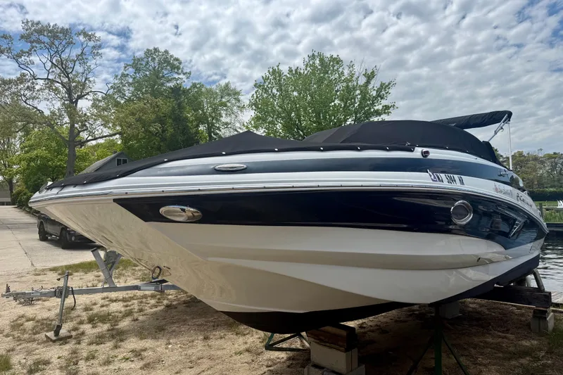 Slide: The Image of 2020 Crownline Eclipse E235 boat on trailer, covered, with trees in the background. - 15