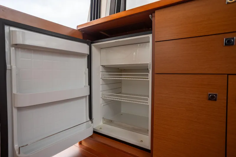 Slide: The Image of Open refrigerator in 2017 Jeanneau NC 14 yacht interior, showcasing wooden cabinetry. - 12