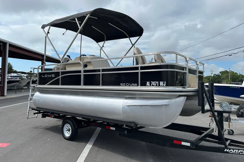 The Image of 2023 Lowe Ultra 162 Fish & Cruise pontoon boat on trailer, parked outdoors. - 1