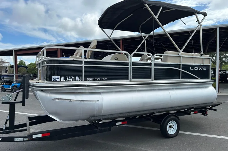 Slide: The Image of 2023 Lowe Ultra 162 Fish & Cruise pontoon boat on trailer, parked outdoors. - 5
