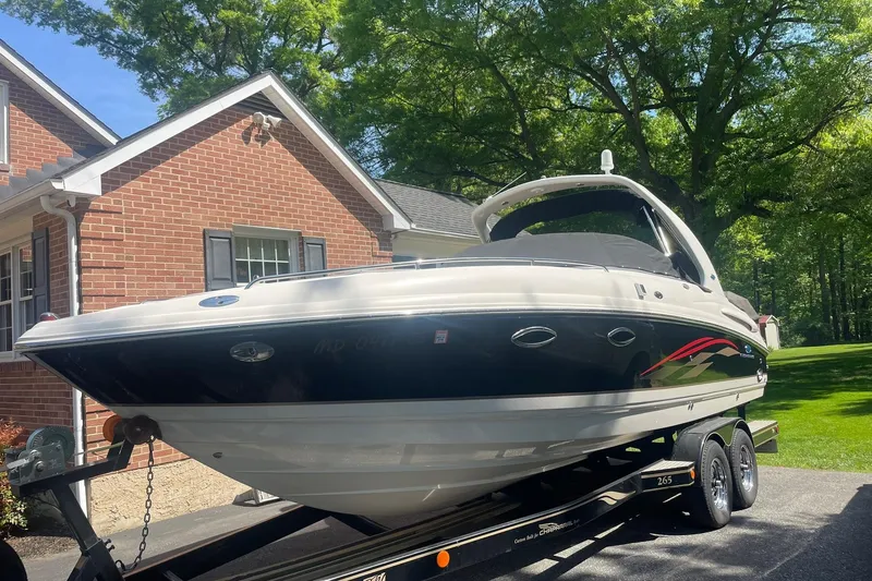 The Image of 2005 Chaparral 265 SSi boat on trailer beside brick house, surrounded by trees. - 0