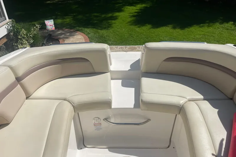 Slide: The Image of 2005 Chaparral 265 SSi boat interior with beige seating and lush green background. - 13