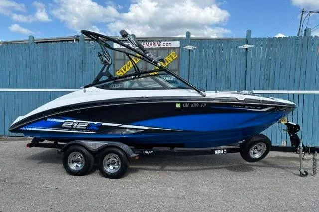 The Image of 2016 Yamaha Boats 212X on trailer, blue and white, parked by blue fence. - 0