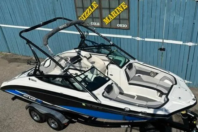 Slide: The Image of 2016 Yamaha Boats 212X on trailer, parked near blue building. - 6