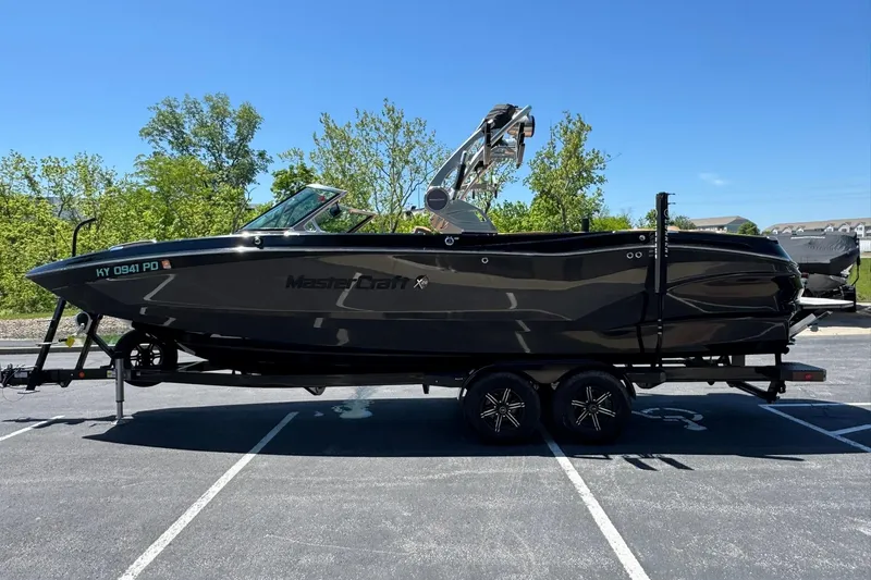 Slide: The Image of 2021 MasterCraft X26 boat on trailer in parking lot, sunny day, trees in background. - 5