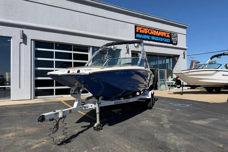 The Image of 2010 MasterCraft XStar boat on trailer outside Performance Marine Watersports store. - 1
