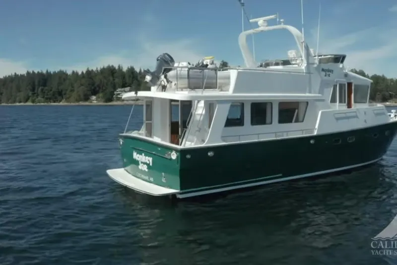 Slide: The Image of 2003 Jefferson Pilothouse 53 yacht on calm water, forested shoreline in background. - 2