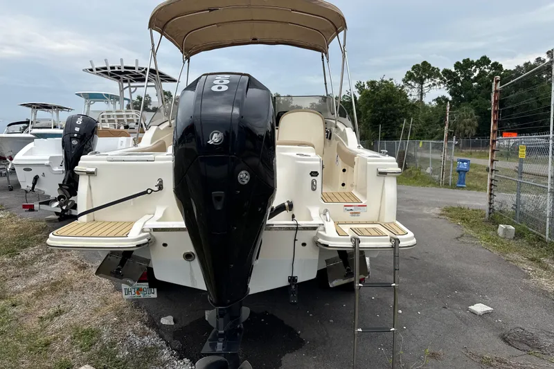 Slide: The Image of 2023 Scout 215 Dorado boat with outboard motor and canopy, parked on pavement. - 3