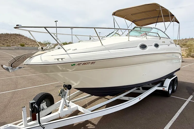 The Image of 1999 Sea Ray Sundancer 260 boat on trailer in parking lot, featuring sleek design and canopy. - 0