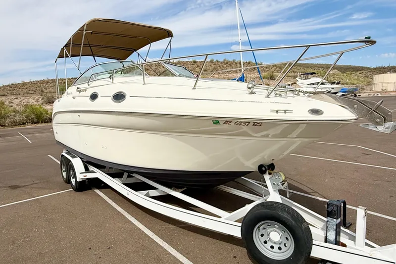 Slide: The Image of 1999 Sea Ray Sundancer 260 boat on trailer, parked in a lot under a clear sky. - 1