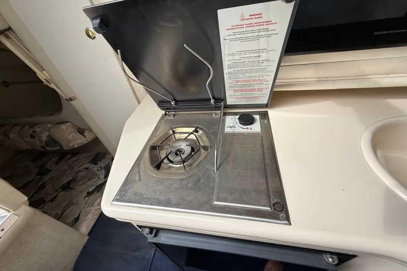 Slide: The Image of 1999 Sea Ray Sundancer 260 interior stove and sink area, showcasing compact kitchen amenities. - 19
