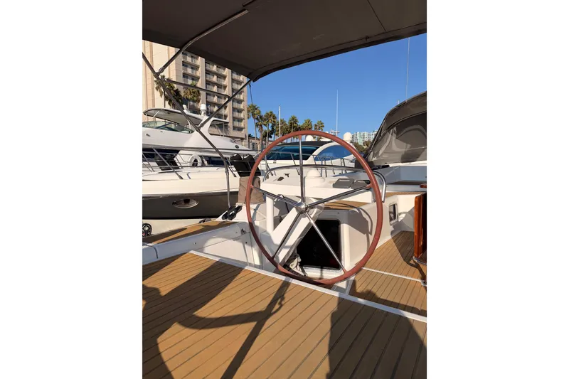 Slide: The Image of 2013 Jeanneau 57 yacht helm with wooden deck, docked in marina under clear blue sky. - 17