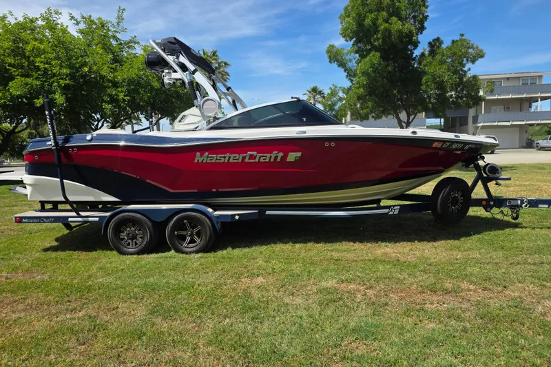 The Image of 2019 MasterCraft XT23 boat on trailer, parked on grass with trees in background. - 0