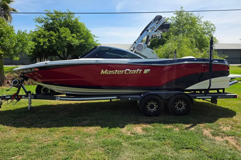 Slide: The Image of 2019 MasterCraft XT23 boat on trailer, red and white, parked on grass. - 3