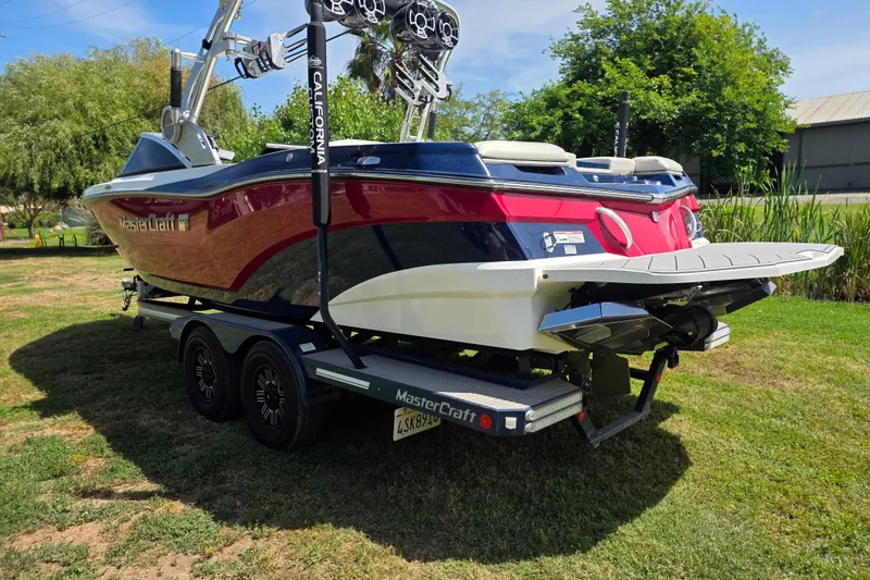 Slide: The Image of 2019 MasterCraft XT23 boat on trailer, parked on grass with trees in background. - 4