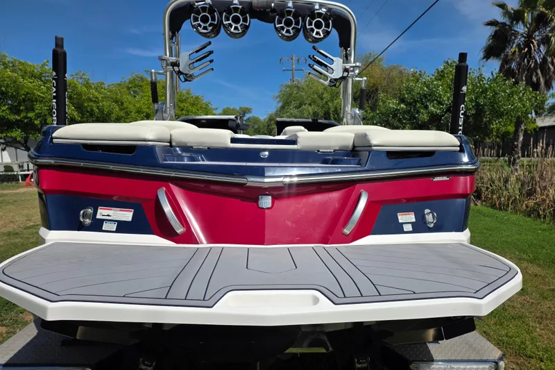 Slide: The Image of 2019 MasterCraft XT23 boat with red and blue exterior, rear view, parked on grass. - 5