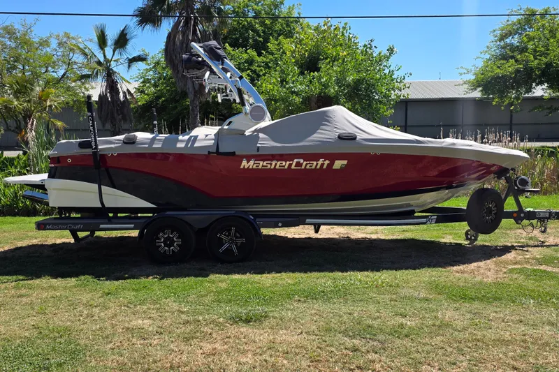 Slide: The Image of 2019 MasterCraft XT23 boat on trailer, covered, parked on grass with trees in background. - 7