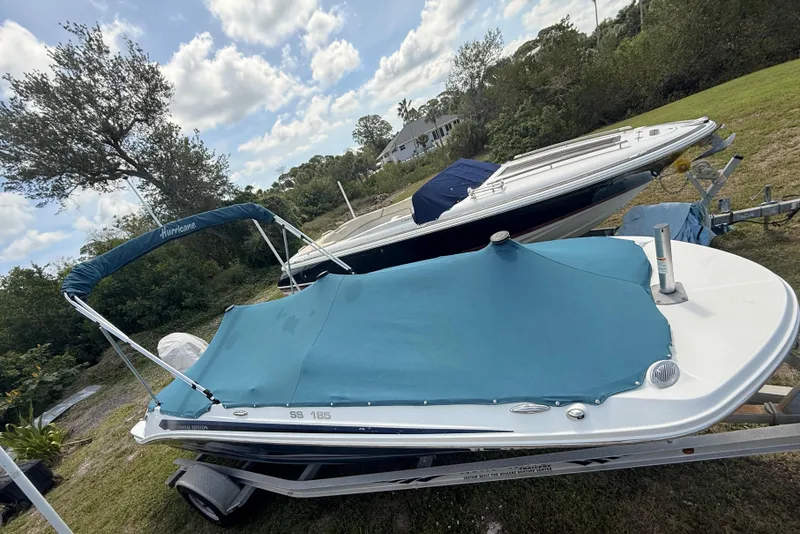 Slide: The Image of 2020 Hurricane SunDeck Sport 185 OB boat with blue cover on trailer, parked on grass. - 25