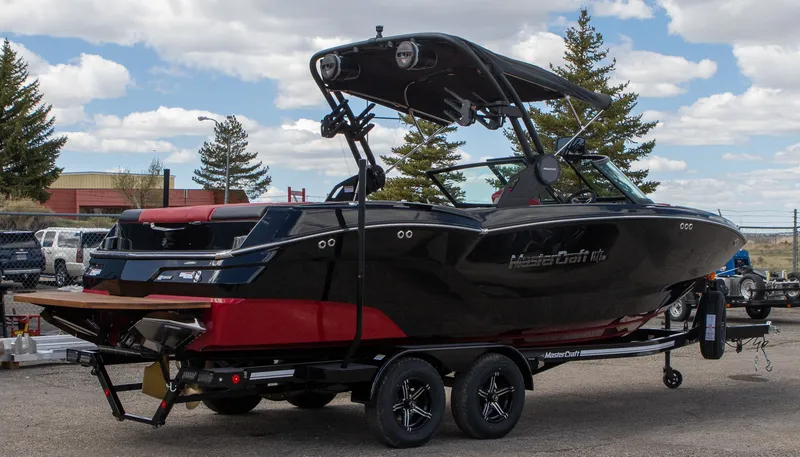 Slide: The Image of 2024 MasterCraft NXT23 boat on trailer, black and red, parked outdoors. - 2