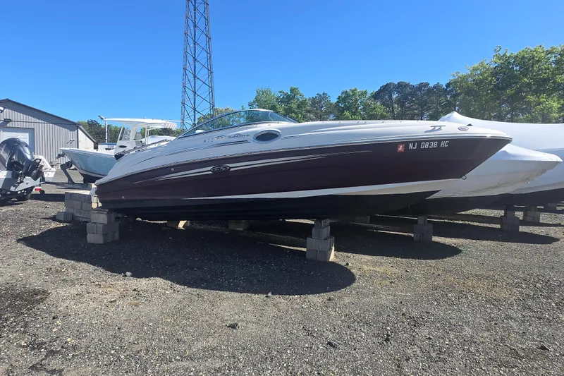 Slide: The Image of 2009 Sea Ray 240 Sundeck boat on blocks, parked outdoors under clear blue sky. - 18