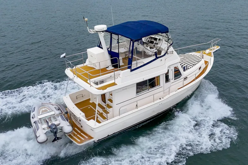 Slide: The Image of 2011 Mainship 395 Trawler cruising on open water with blue canopy and dinghy attached. - 15