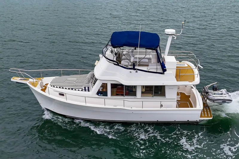 Slide: The Image of 2011 Mainship 395 Trawler cruising on open water, featuring a blue canopy and striped seating. - 16