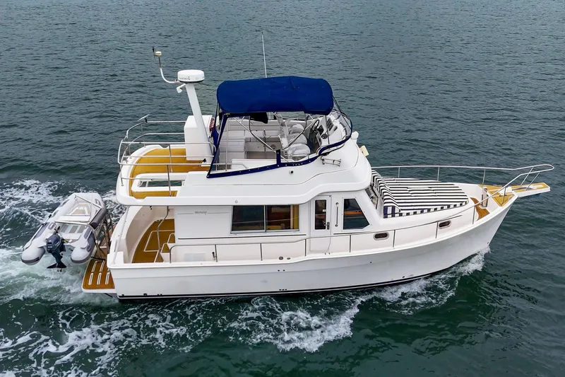 Slide: The Image of 2011 Mainship 395 Trawler cruising on open water with a small dinghy attached. - 17