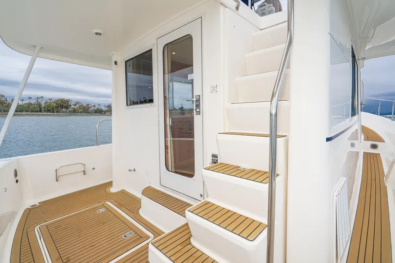 Slide: The Image of 2011 Mainship 395 Trawler deck with stairs, featuring teak flooring and waterfront view. - 38