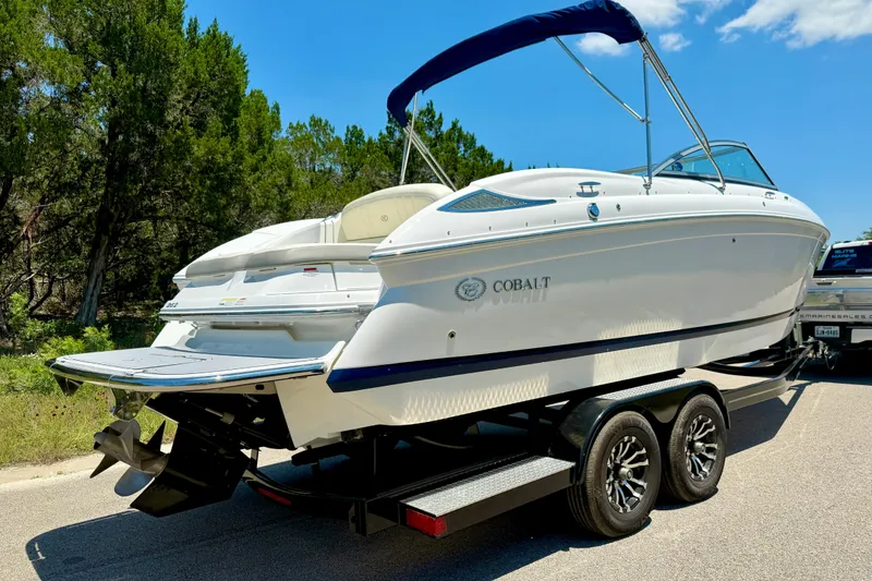 Slide: The Image of 2013 Cobalt 262 boat on trailer, parked on a sunny road with trees in background. - 11