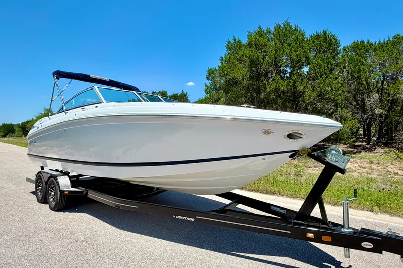 Slide: The Image of 2013 Cobalt 262 boat on trailer, parked on road, surrounded by trees under clear blue sky. - 12