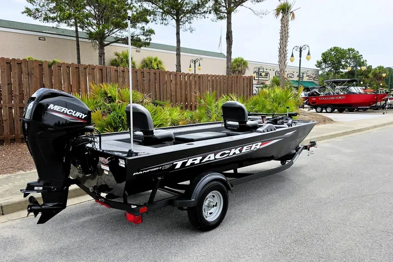 Slide: The Image of 2026 Tracker Panfish 17 boat with Mercury engine, parked outdoors near greenery. - 2