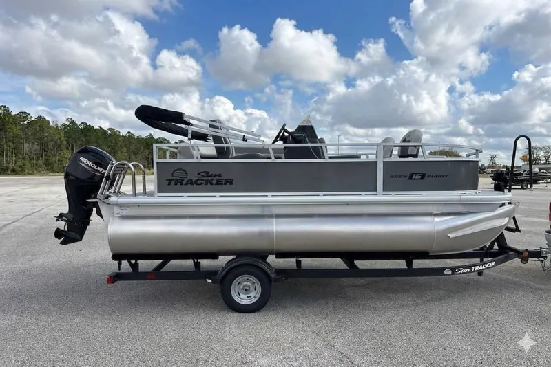 The Image of 2026 Sun Tracker Bass Buggy 16 XL Select pontoon boat on trailer, parked outdoors. - 0