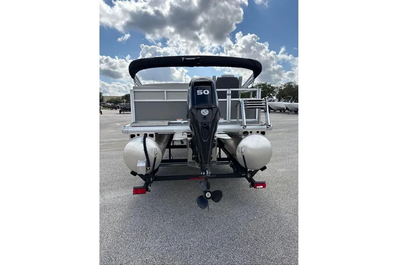 Slide: The Image of 2026 Sun Tracker Bass Buggy 16 XL Select pontoon boat, rear view with motor, under cloudy sky. - 2