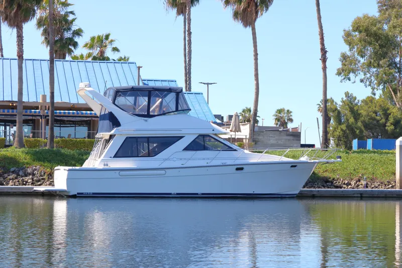 Slide: The Image of 1999 Bayliner 3988 Command Bridge Motoryacht docked by palm trees and modern buildings. - 2